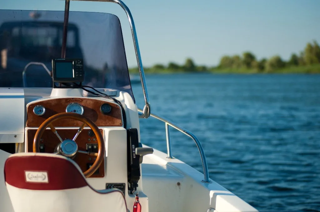 View from a small motorboat helm over blue water, with a wooden steering wheel, chrome gauges and a GPS unit on the console